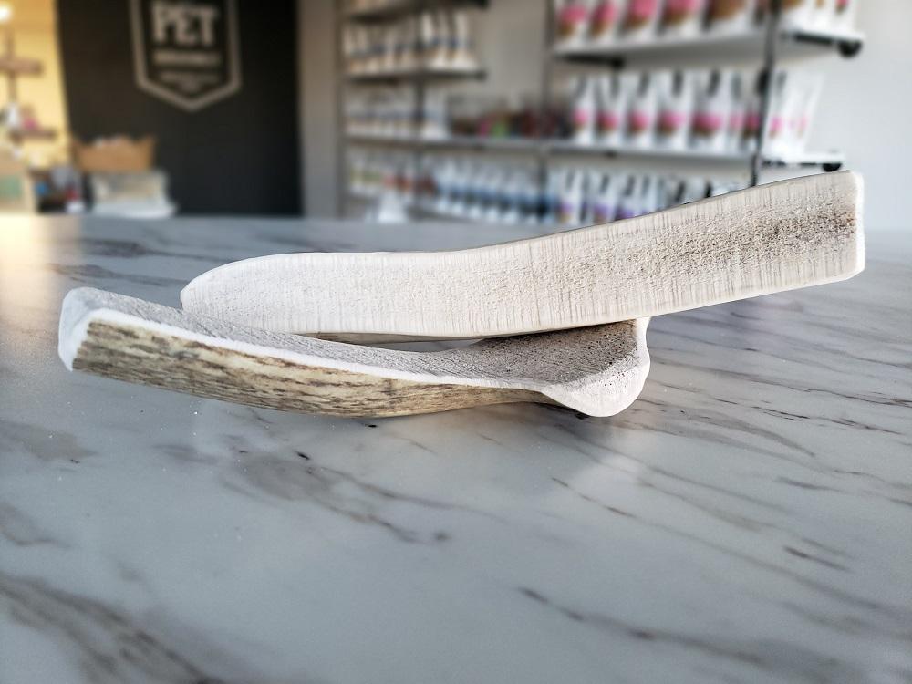 Medium split elk antler dog chew laid on marble countertop in pet store background