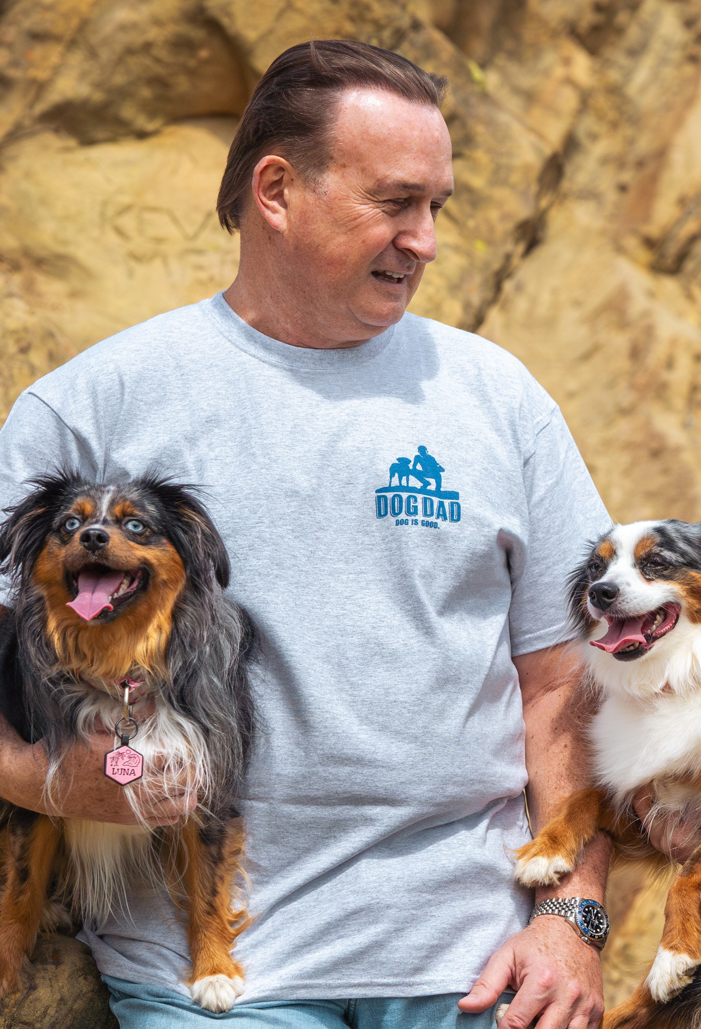 Man wearing grey Dog Dad T-Shirt holding two dogs outdoors