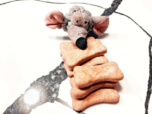 Stack of crunchy cheddar paw bone dog treats with a plush mouse toy on white marble background