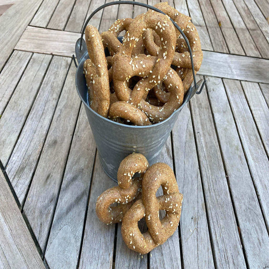 Bucket of organic parmesan pretzels dog treats sprinkled with sesame seeds on wooden table