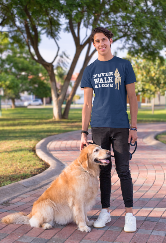 Man wearing navy Never Walk Alone t-shirt standing with golden retriever dog outdoors on a sunny day