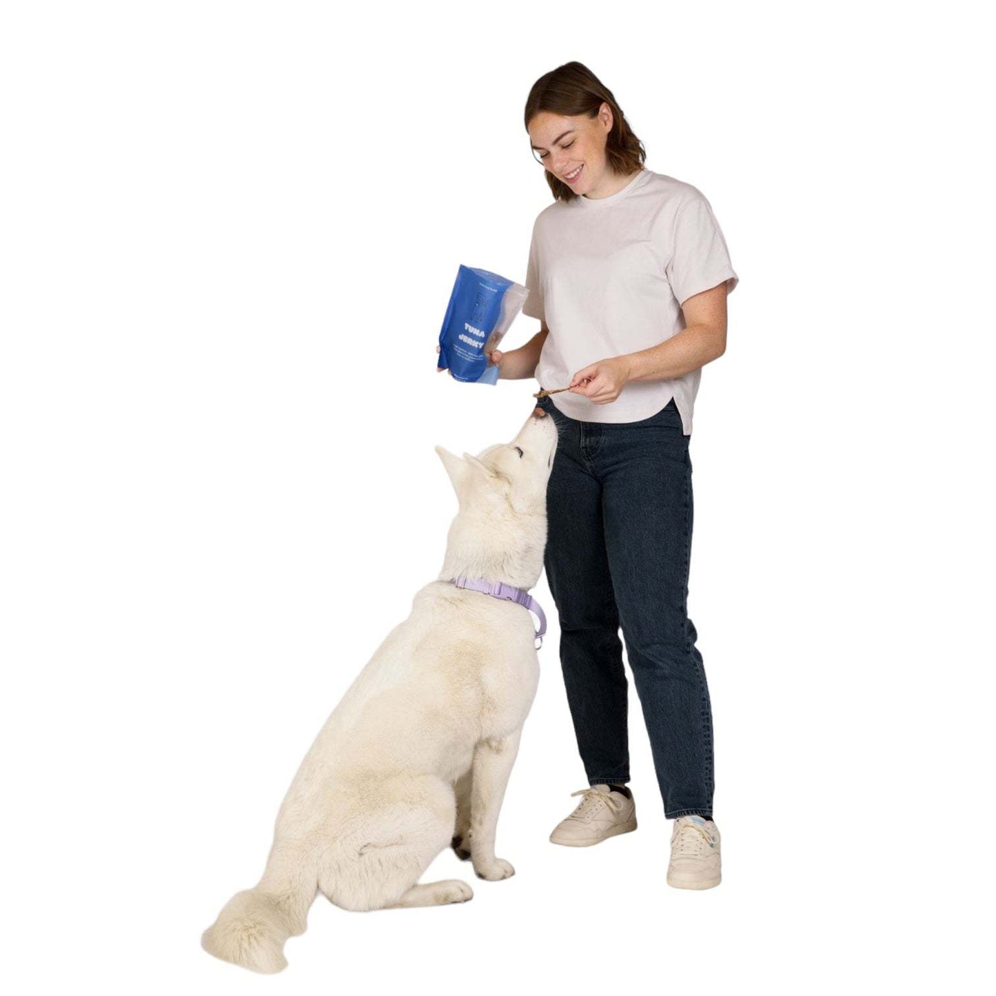Woman feeding white dog Tuna Jerky Dog Treats from blue bag