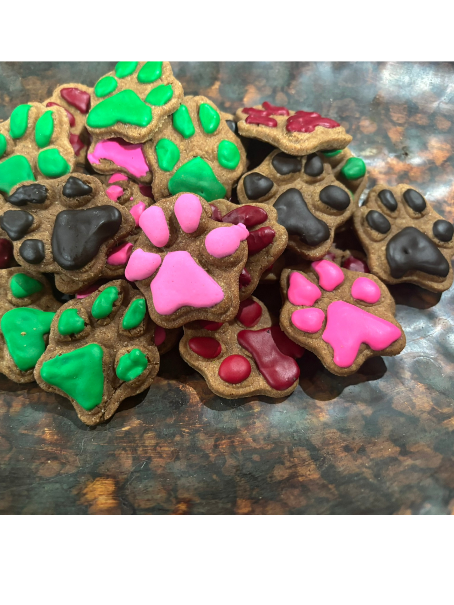 Assorted frosted paw-shaped organic peanut butter dog treats with colorful frosting on a rustic surface