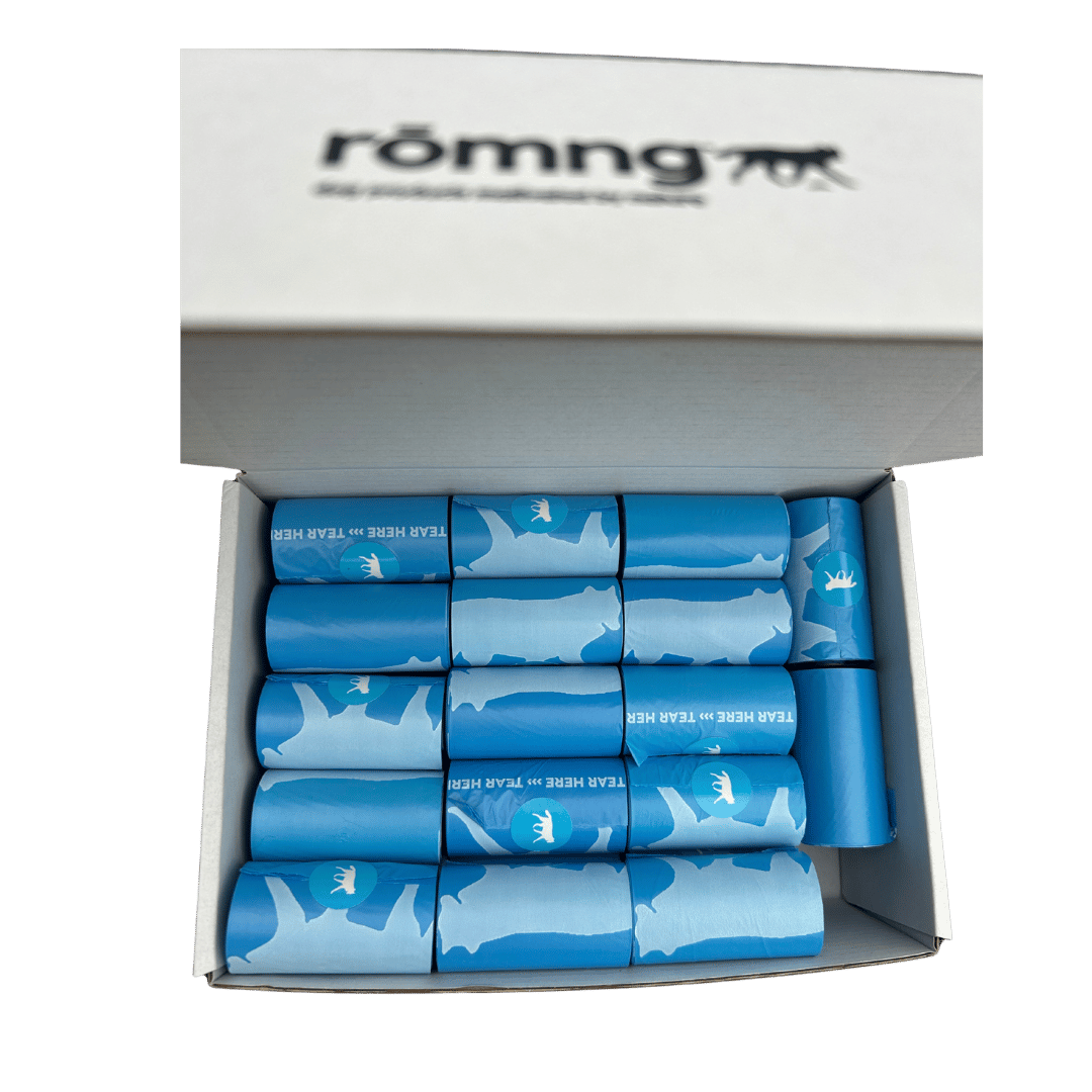 Open box of blue bio-based dog poop bags rolls with white dog silhouettes and tear tab, branded rōmng, eco-friendly pet waste solution