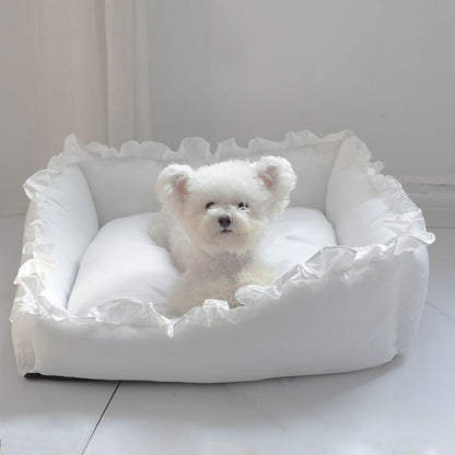 Small white plush princess dog bed sofa with ruffled edges and a small white dog sitting inside