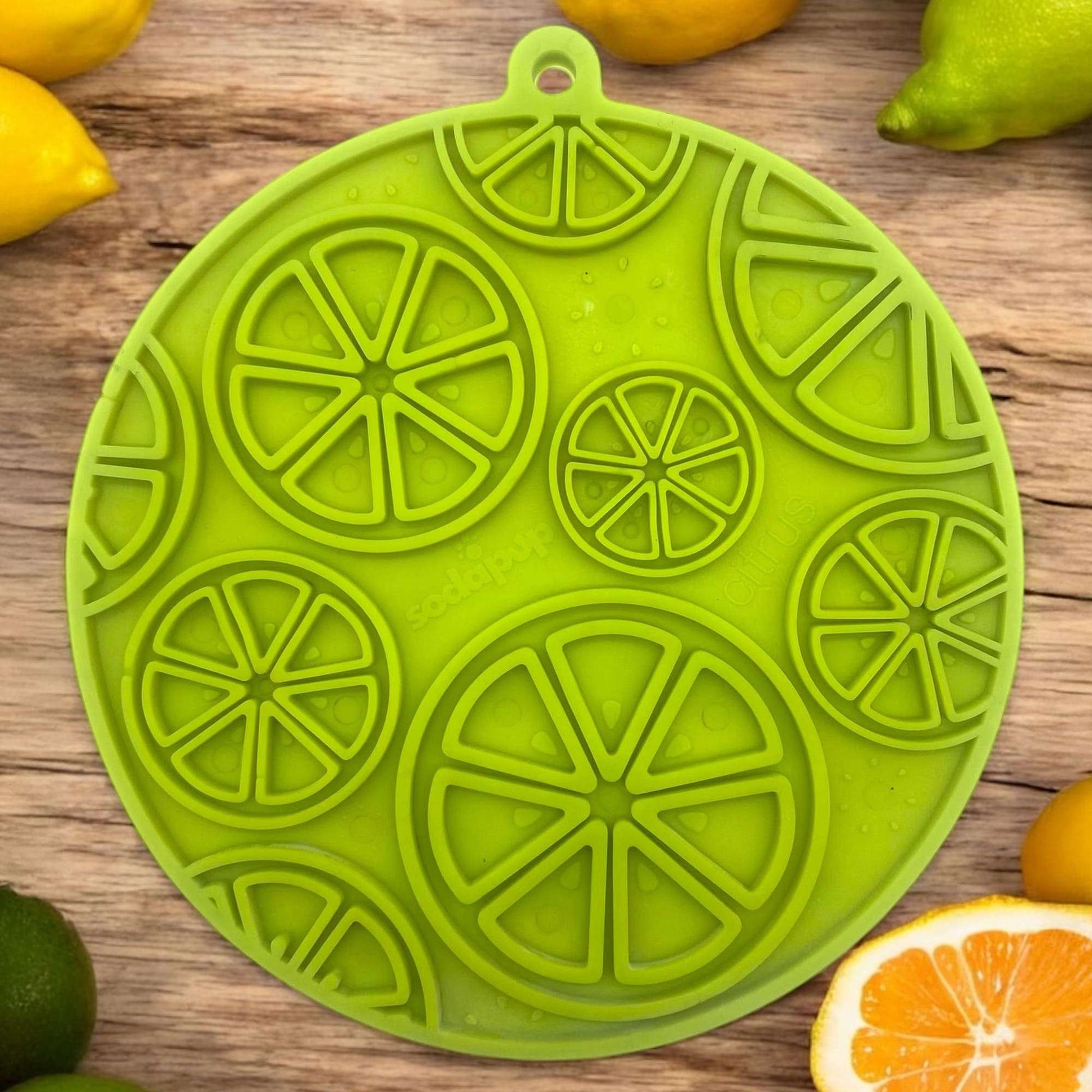 Citrus patterned green enrichment lick mat with suction cups for dogs and cats on wooden surface with citrus fruits background