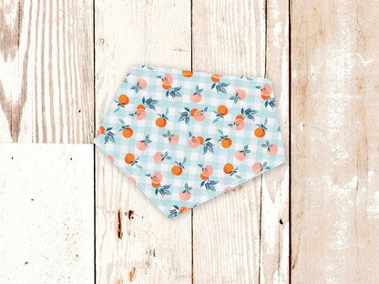 Gingham Peaches dog bandana with peach print and adjustable snap closures on white flannel backing