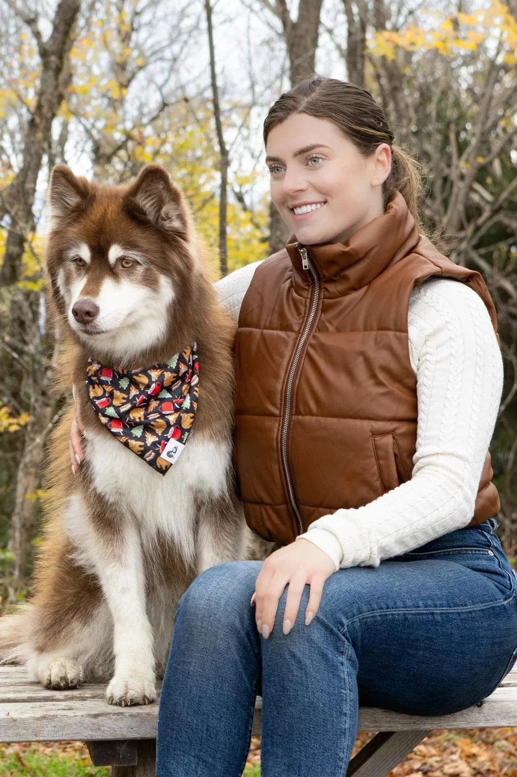 Dog wearing Woodland Tales Dog Bandana with autumn leaves pattern sitting beside smiling woman outdoors