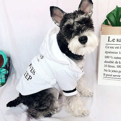 Small dog wearing white bath robe with hood and black text design sitting indoors