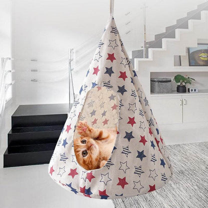 Conical pet hammock with star print hanging indoors, featuring an orange kitten inside.