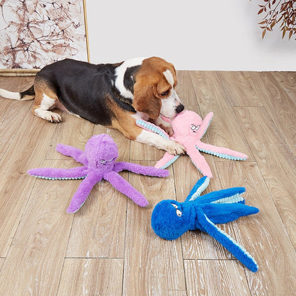 Octopus-shaped indestructible plush squeaky dog toys in purple, pink, and blue colors on wooden floor with a dog playing