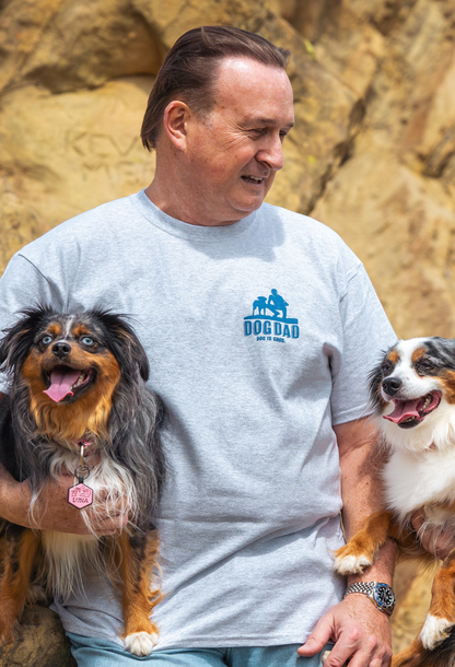 Man wearing grey Dog Dad T-Shirt holding two dogs outdoors