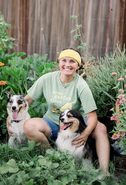 Person wearing green "Never Garden Alone" t-shirt sitting in garden with two dogs