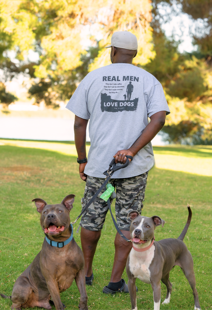 Man wearing a gray "Real Men Love Dogs" T-shirt walking two dogs in a park