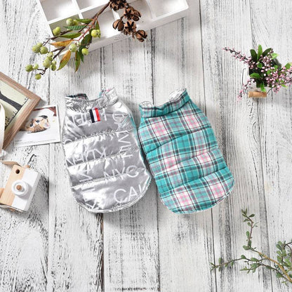 Two autumn and winter dog clothes wear vests for small dogs, one silver with text and one turquoise plaid, displayed on wooden floor.