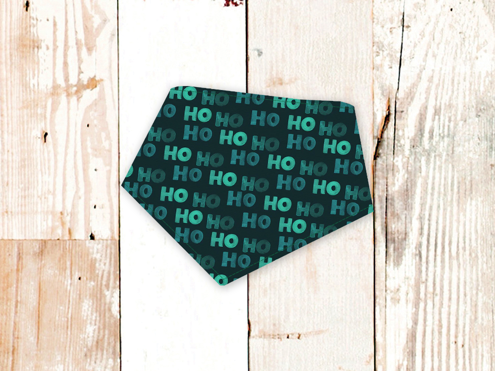 Green HoHoHo dog bandana with adjustable snap closures and flannel backing on wooden background