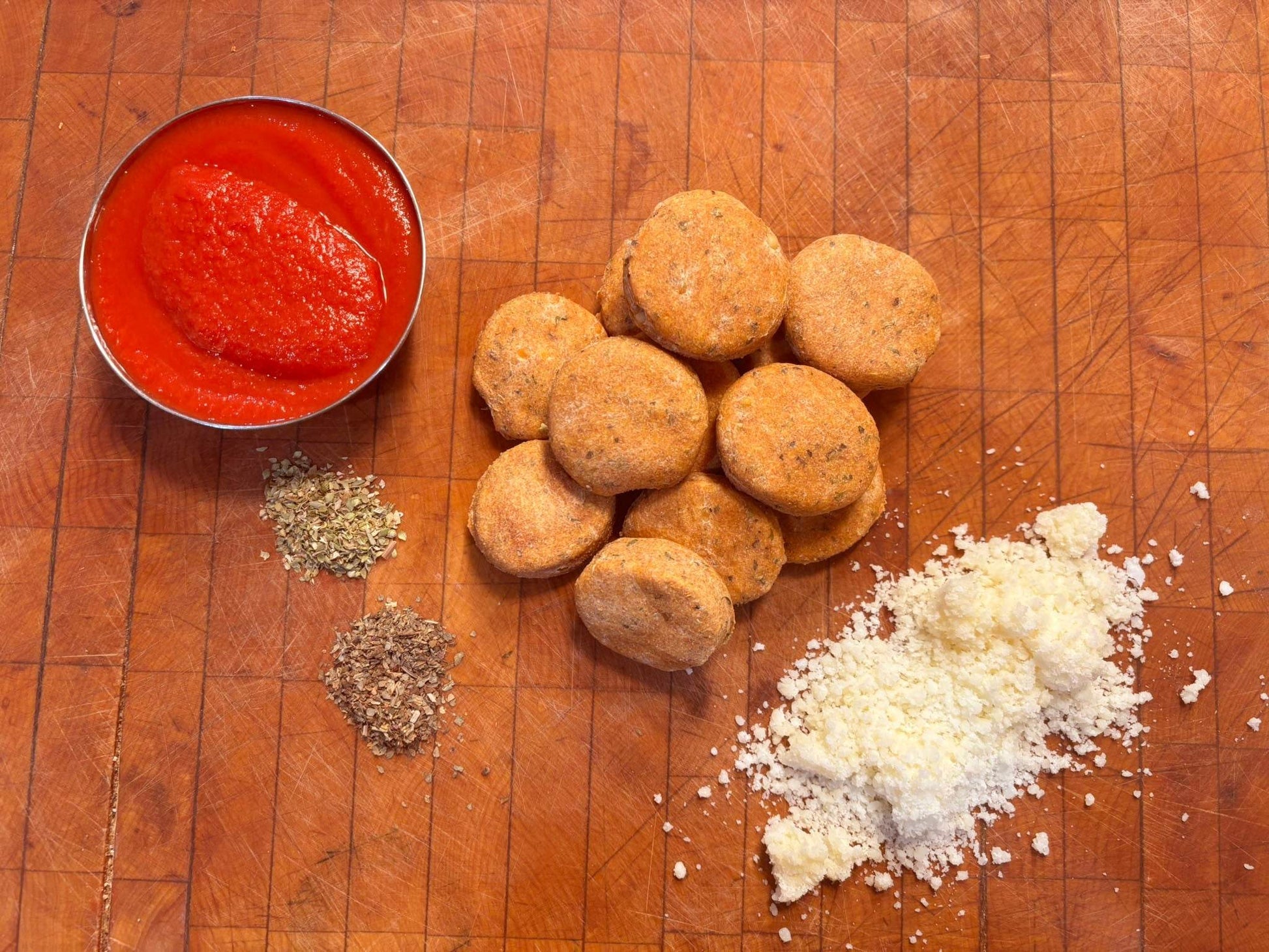 Organic Pizza Paws dog treats with tomato sauce, parmesan cheese, and Italian herbs on wooden cutting board