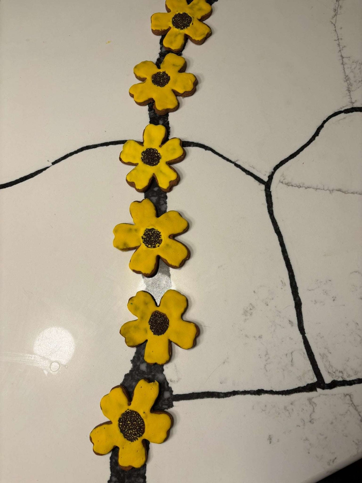 Organic Sunflower Peanut Butter Cookies with yellow glaze and black sesame seed centers arranged on a white surface.