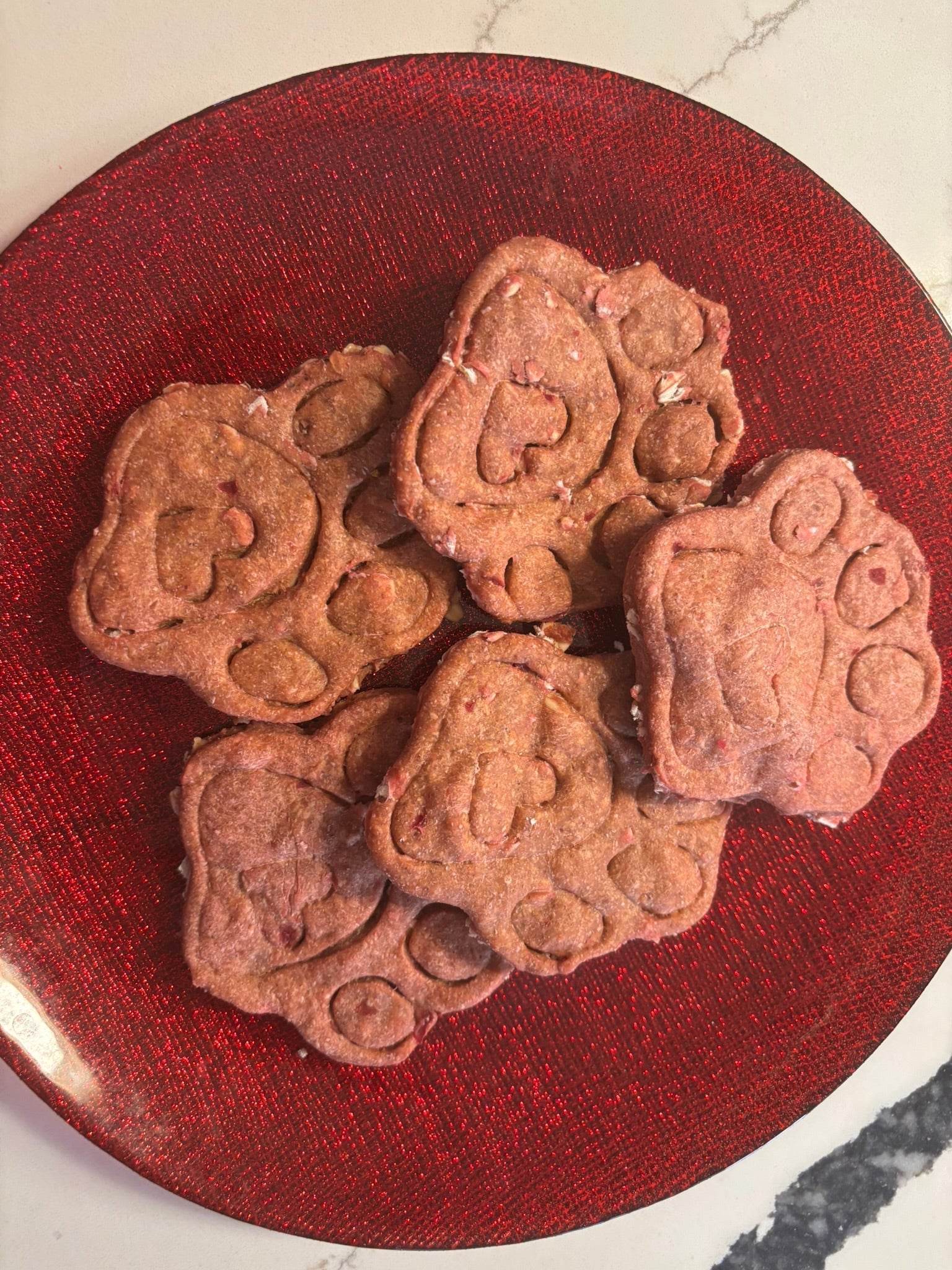Crunchy Beet-a-licious Paws organic dog treats made with beets and peanut butter in paw shapes on red plate