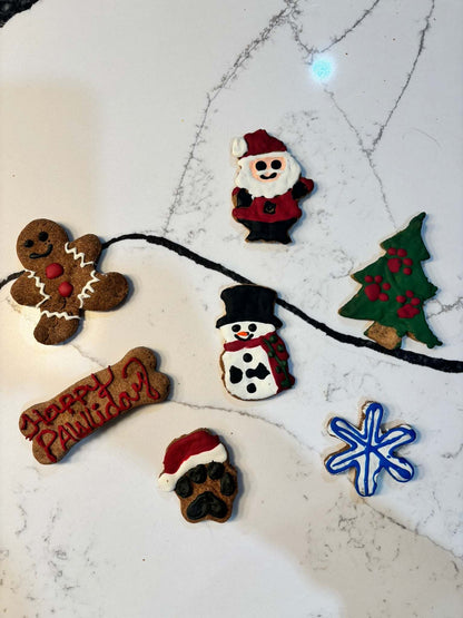 Whimsical Organic Christmas dog cookies in festive shapes including Santa, snowman, tree, snowflake, gingerbread, and paw print with holiday icing.