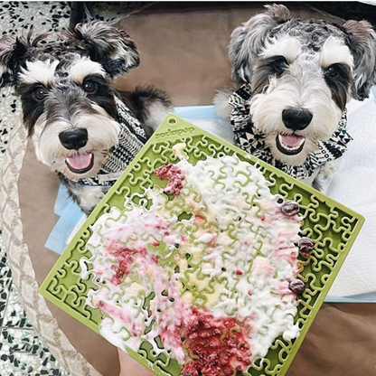 Two dogs licking a green Jigsaw Puzzle eMat filled with yogurt and fruit spread for enrichment and anxiety relief