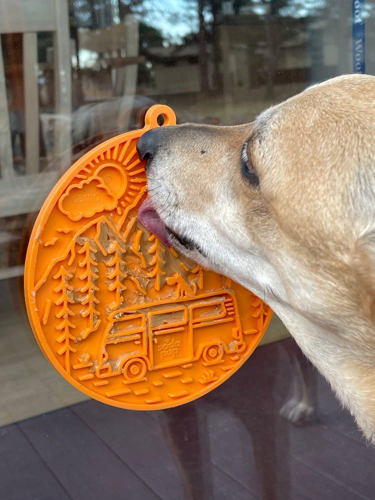 Dog licking orange Camp eMat enrichment lick mat with retro van design attached to glass with suction cups