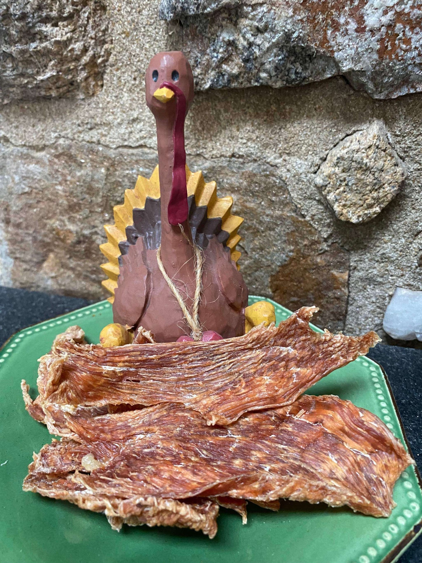 Snarky Bark Turkey Breast Jerky lean protein pet treats on green plate with turkey figurine and stone background