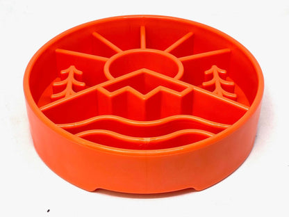 Orange slow feeder dog bowl with raised outdoor design featuring mountains and sun pattern for mental enrichment and slow eating.