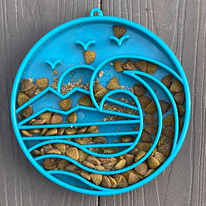 Blue shallow slow feeder dog bowl with Baja-inspired ridges filled with dry dog food on dark surface