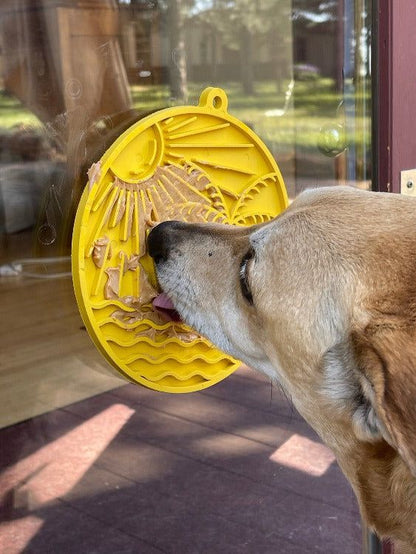 Dog licking yellow Sun n' Sea eMat lick mat with suction cups on glass door