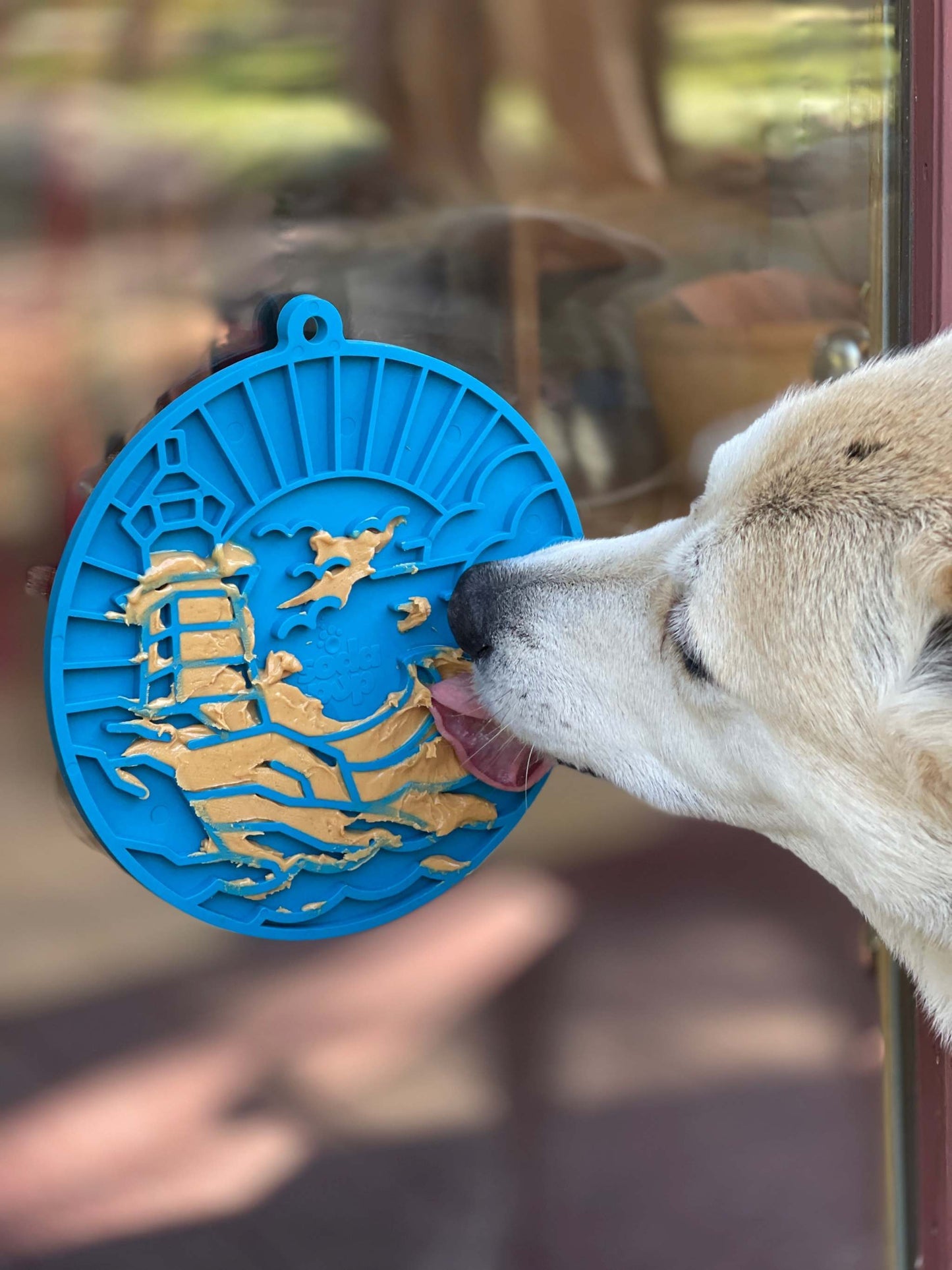 Dog licking blue Lighthouse eMat with suction cups attached to glass door for slow feeding and enrichment