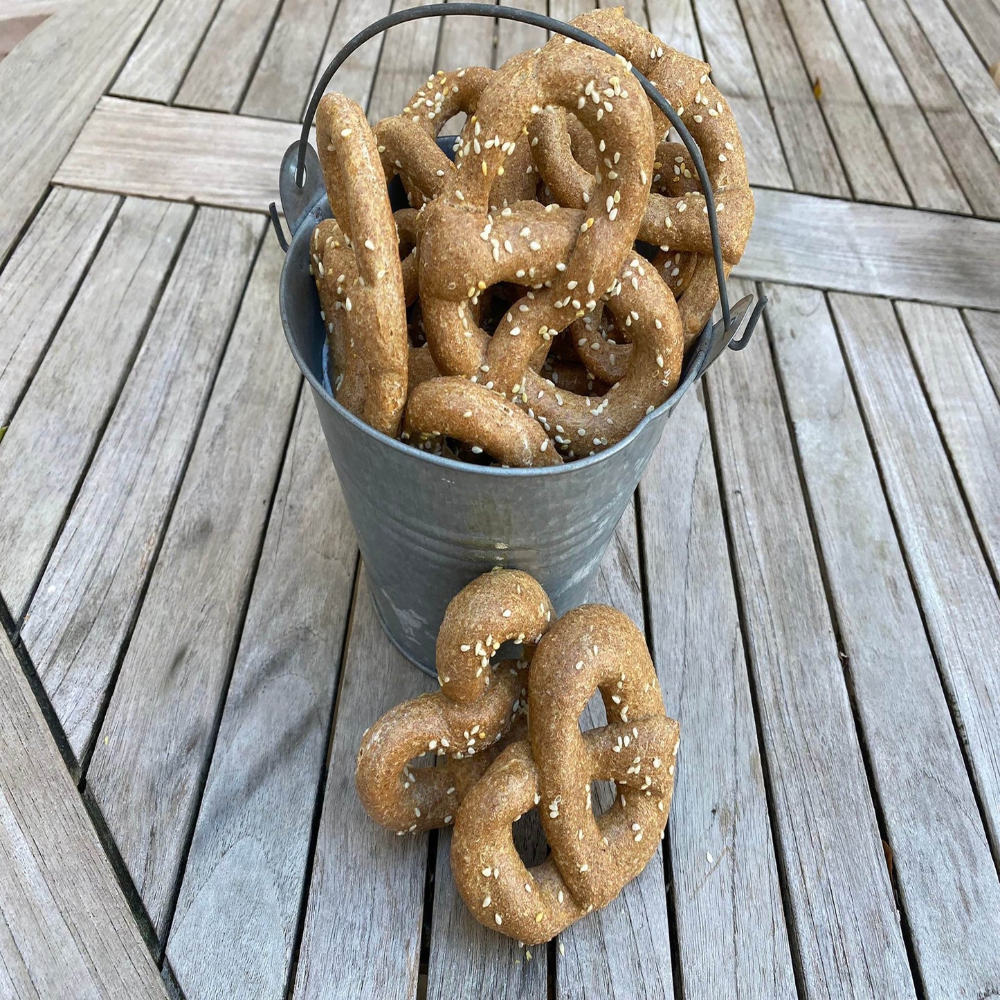 Bucket of organic parmesan pretzels dog treats sprinkled with sesame seeds on wooden table