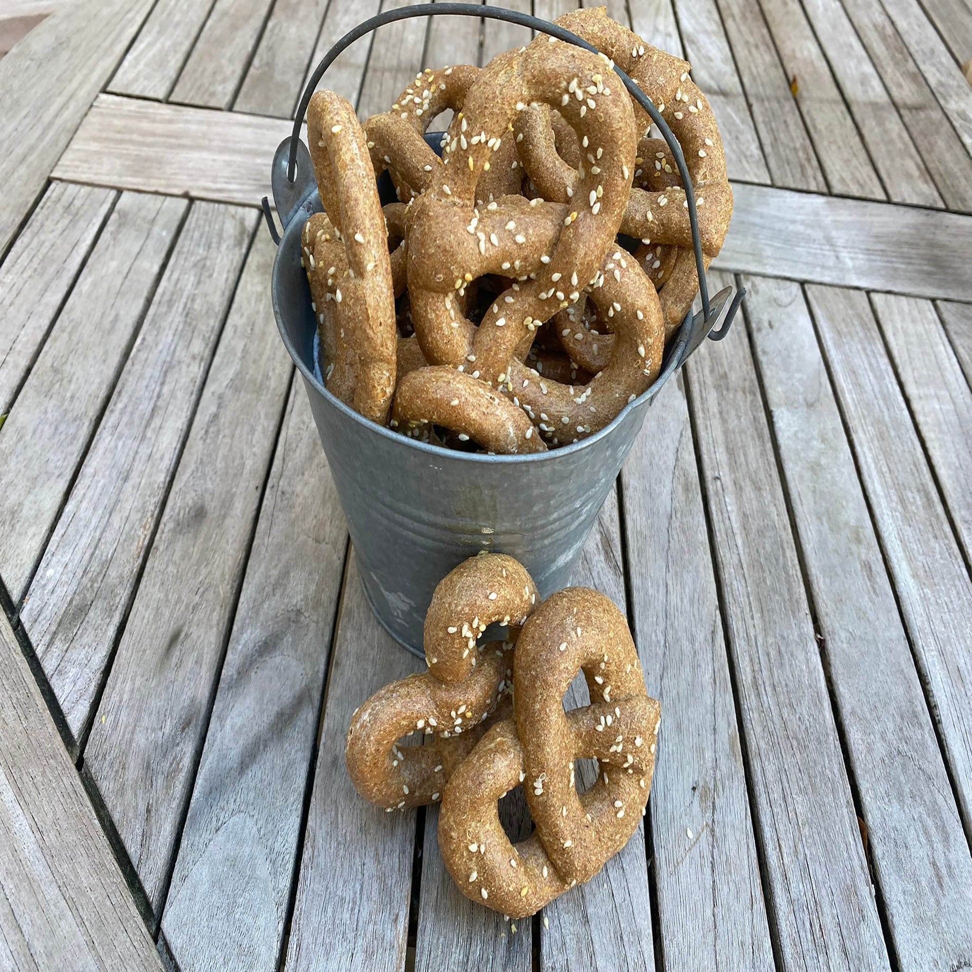 Bucket of organic parmesan pretzels dog treats sprinkled with sesame seeds on wooden table