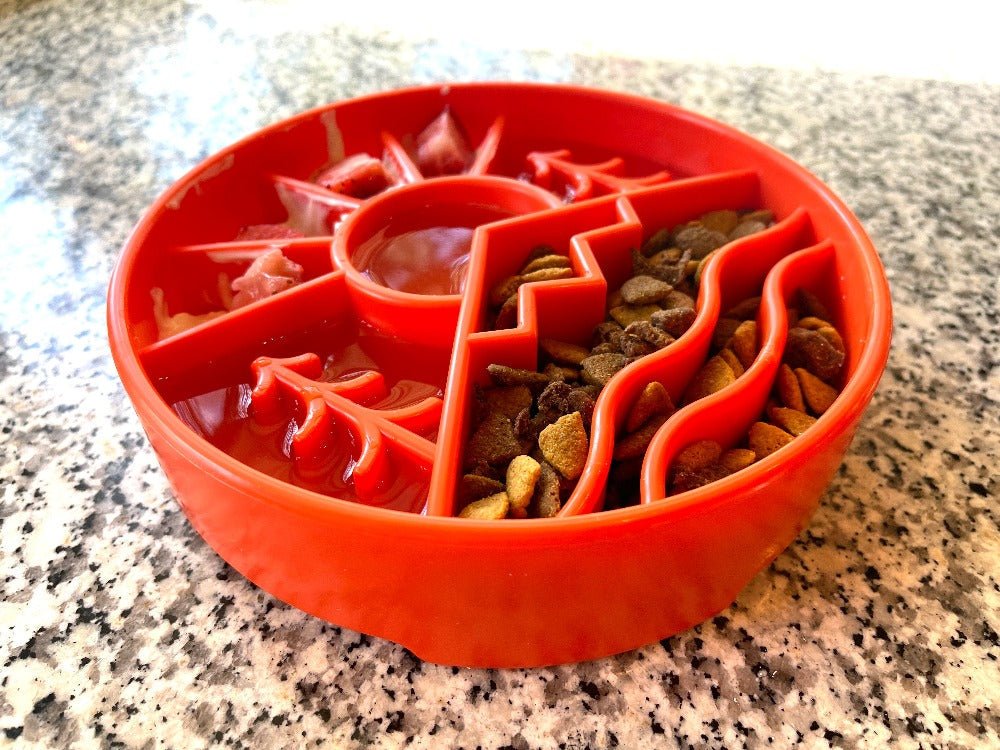 Red slow feeder dog bowl with multiple compartments and raised ridges filled with kibble and wet food on granite countertop