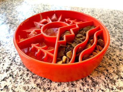 Red slow feeder dog bowl with multiple compartments and raised ridges filled with kibble and wet food on granite countertop