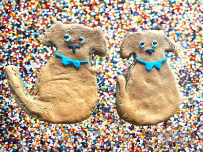 Two dog-shaped Finn Organic Peanut Butter Cookies by Finn's with blue bow ties on colorful sprinkle background