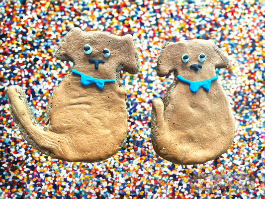Two dog-shaped Finn Organic Peanut Butter Cookies by Finn's with blue bow ties on colorful sprinkle background