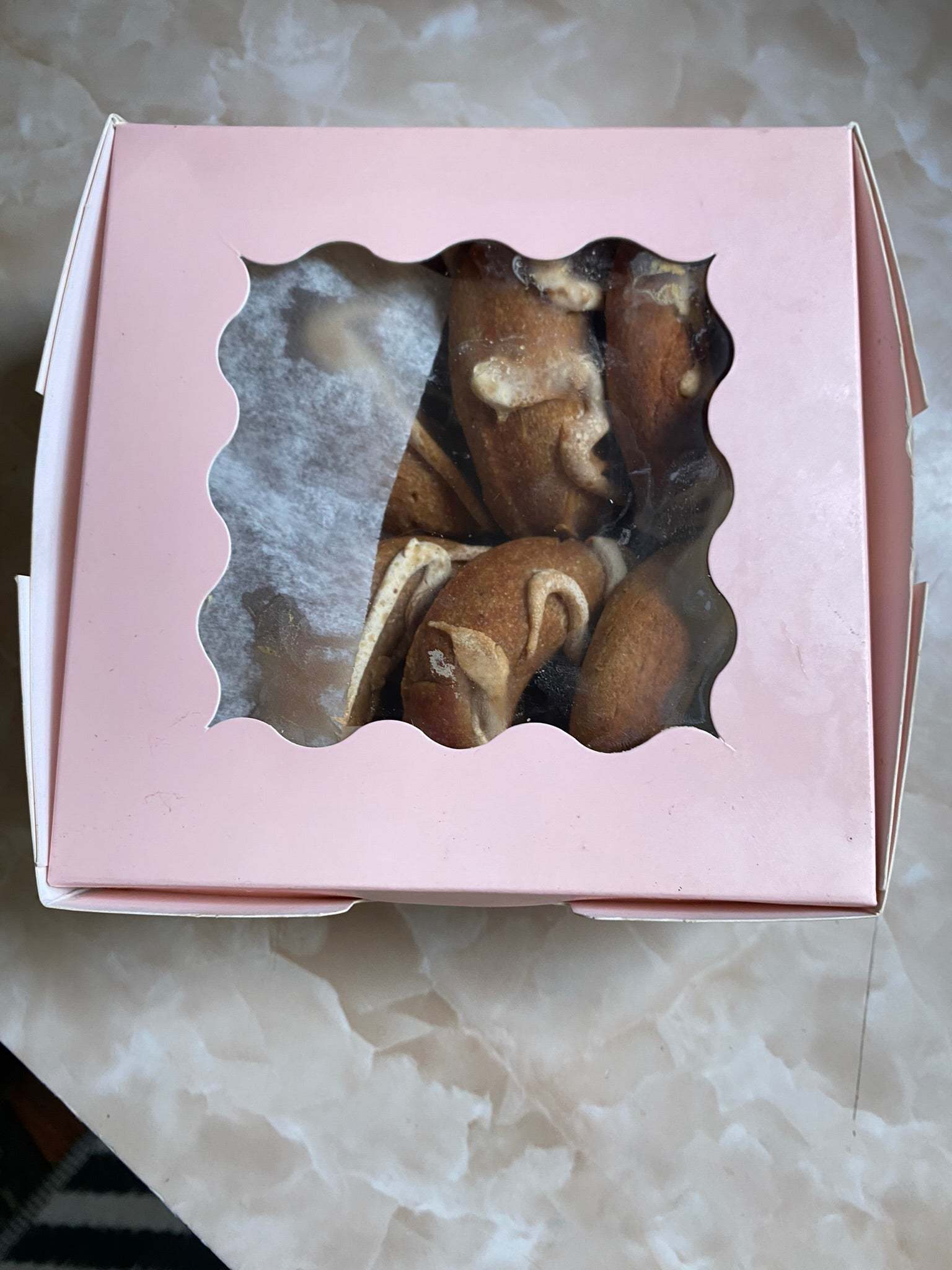 Box of organic peanut butter dog donuts with peanut butter drizzle in pink bakery packaging