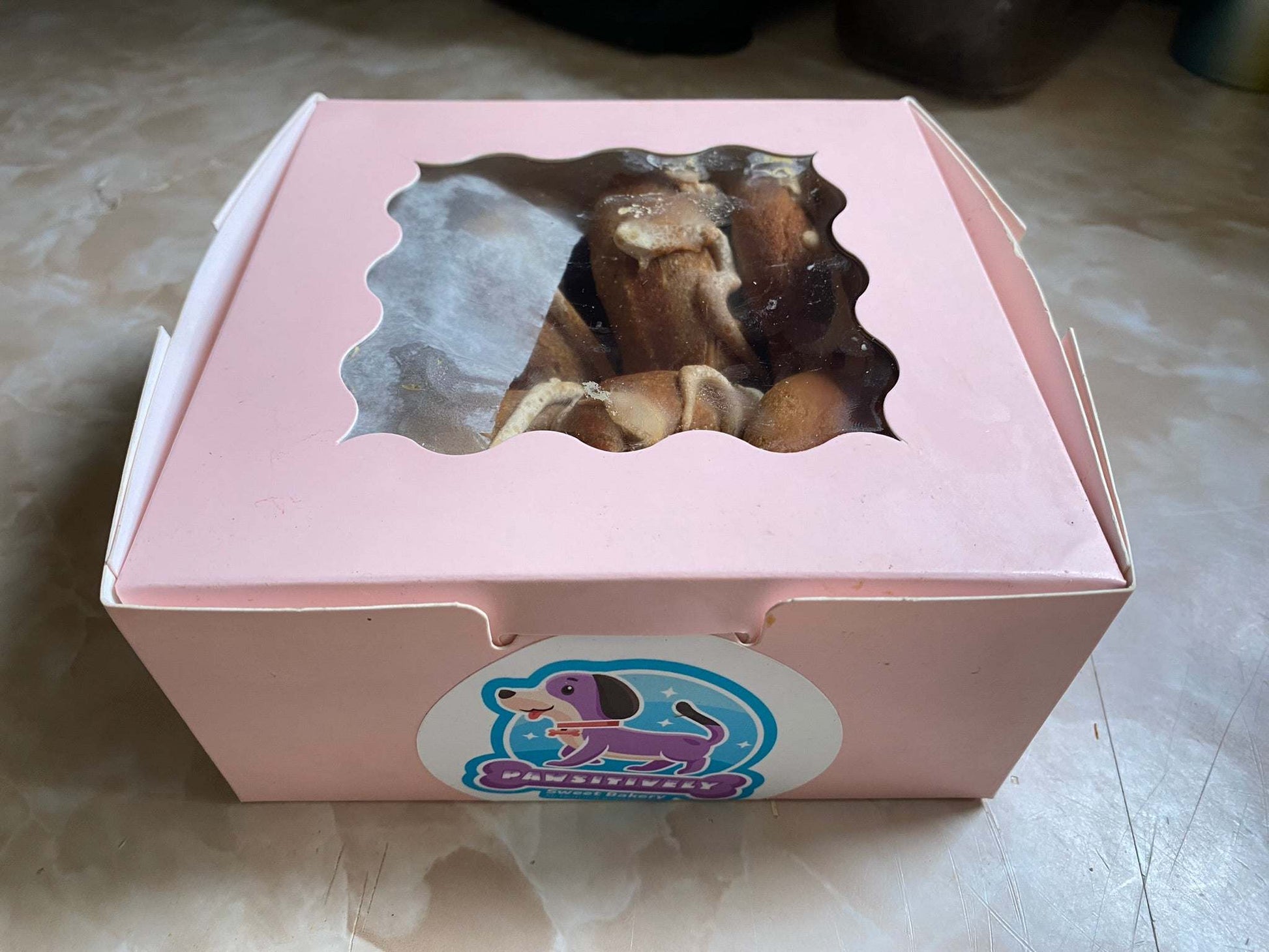 Pink bakery box with organic peanut butter dog donuts inside, packaged for gifting or special occasions