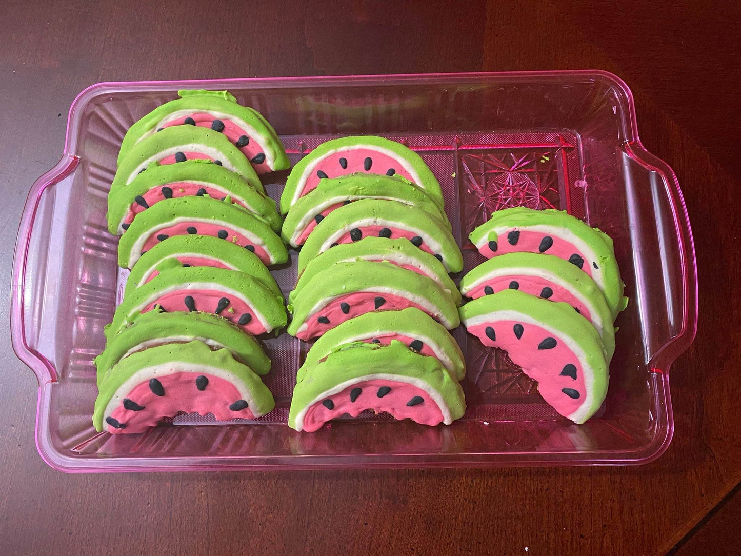 Tray of organic watermelon-shaped dog cookies with pink, white, and green icing and black seed details