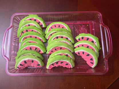 Tray of organic watermelon-shaped dog cookies with pink, white, and green icing and black seed details