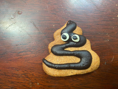 Poop Organic Dog Cookie shaped like poop emoji with chocolate icing eyes and swirl on wooden surface