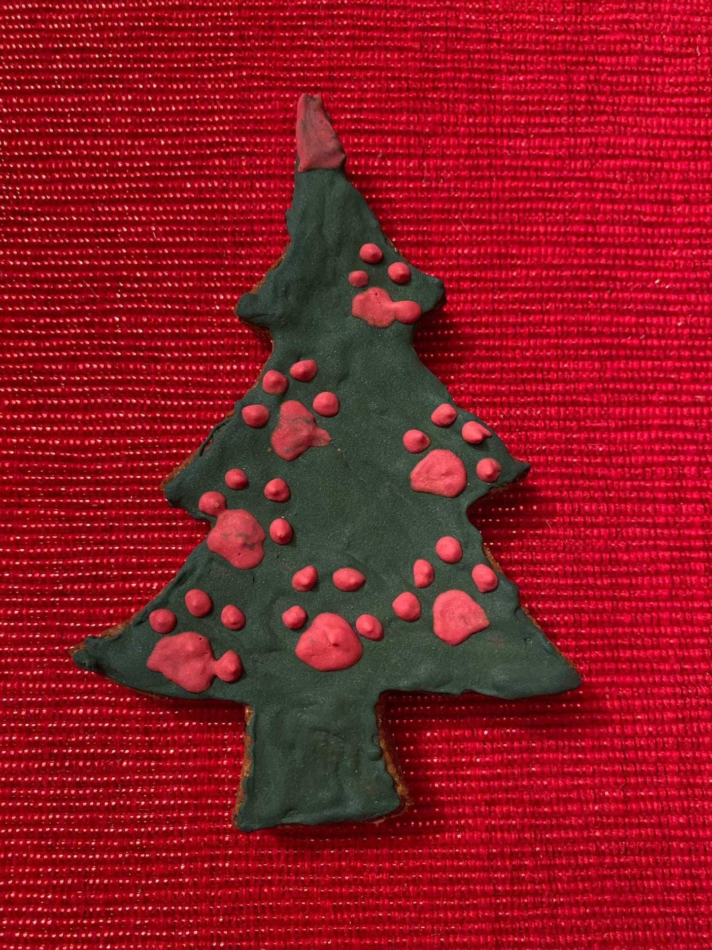 Whimsical Organic Christmas tree shaped organic dog cookie with festive pink icing on red background