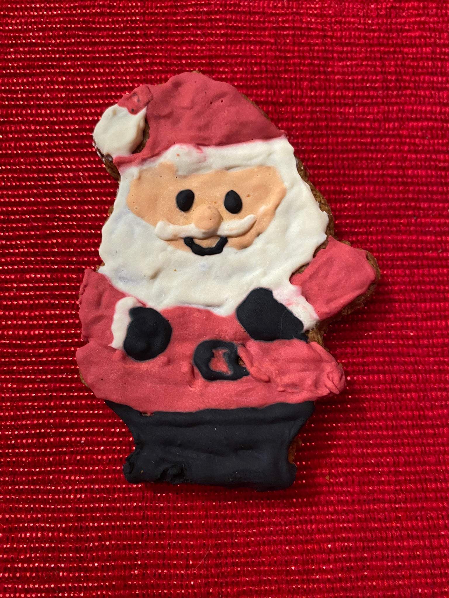 Whimsical Organic Christmas Santa paw dog cookie with festive icing on red background
