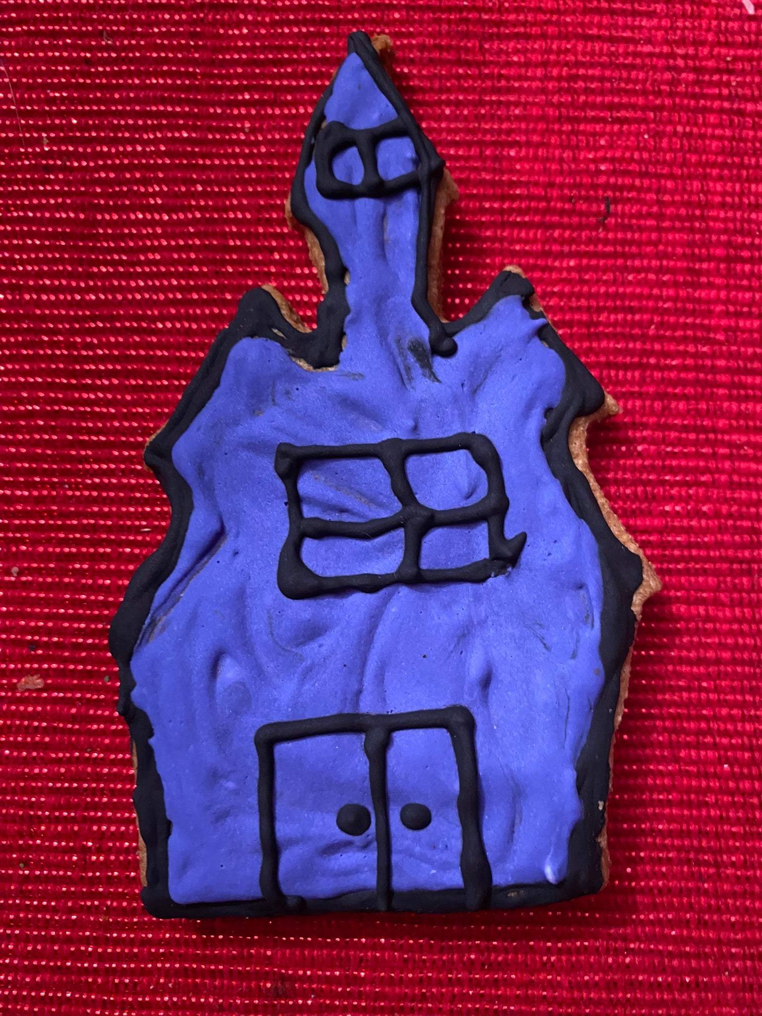 Halloween organic dog cookie shaped like a haunted house with purple icing and black details on red background