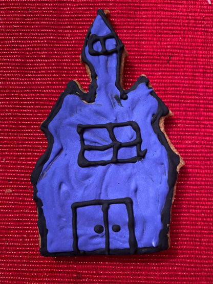 Halloween organic dog cookie shaped like a haunted house with purple icing and black details on red background