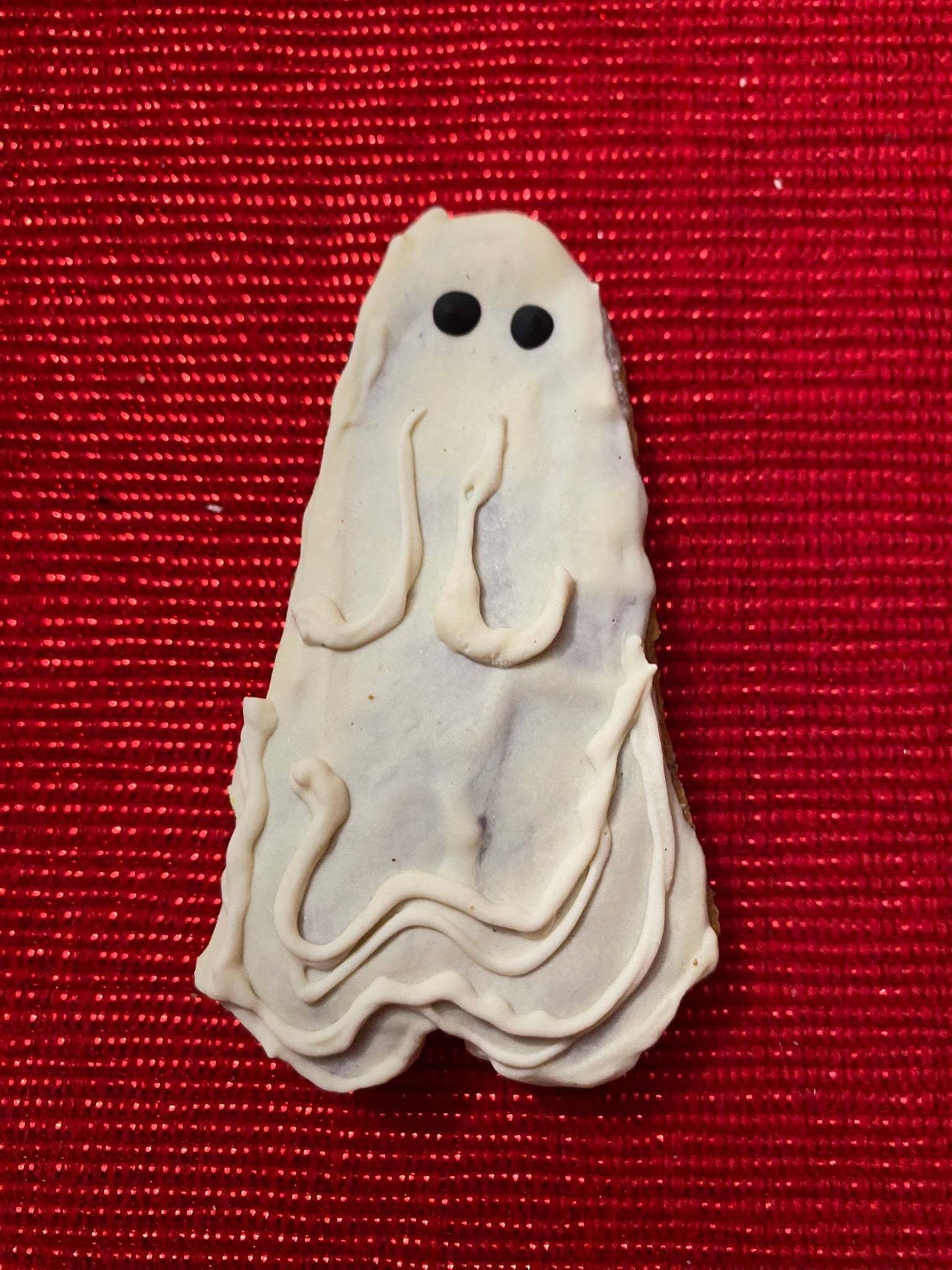 Organic Halloween ghost-shaped dog cookie on red background