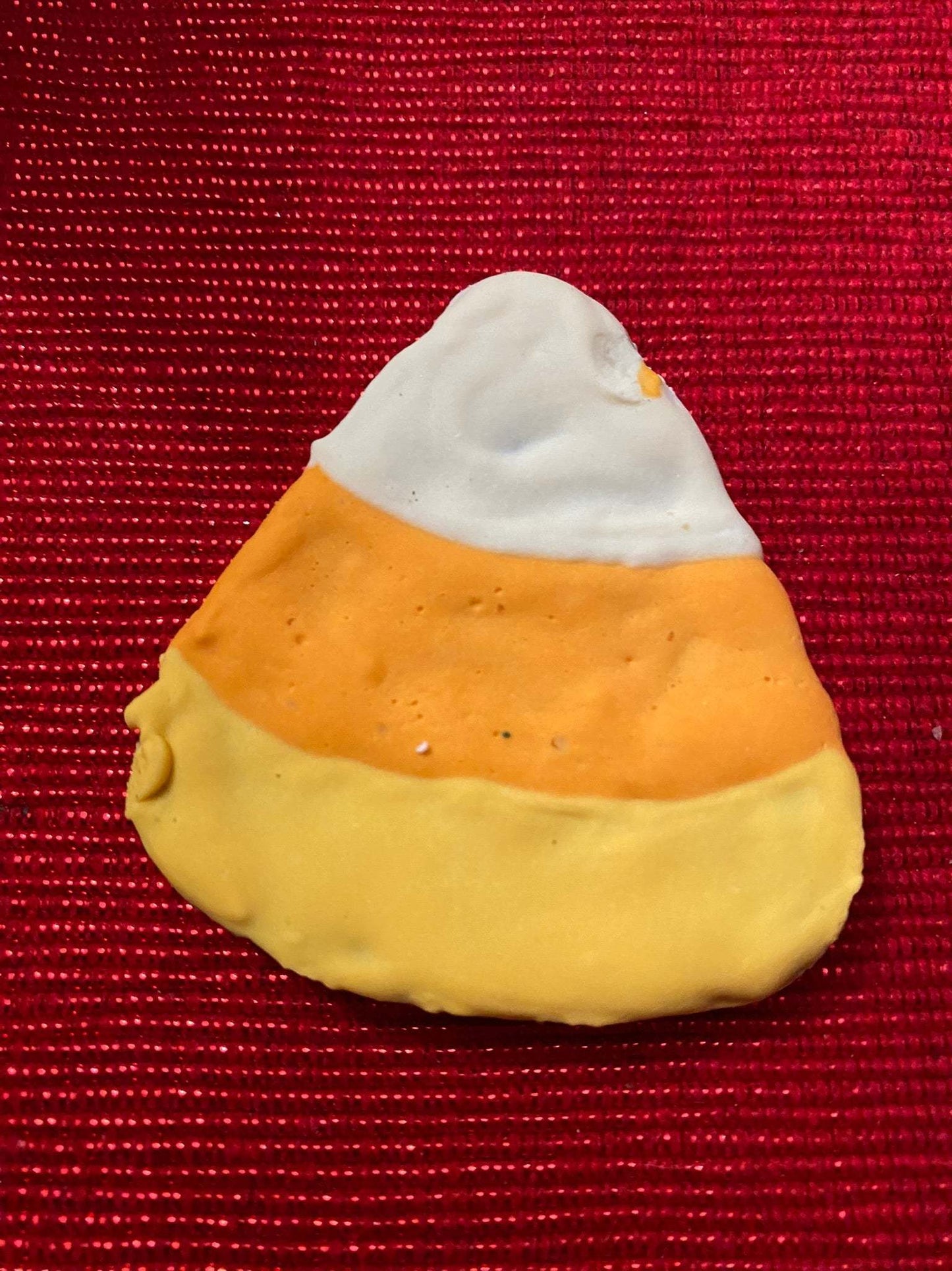 Organic Halloween dog cookie shaped like candy corn with white, orange, and yellow icing on red background
