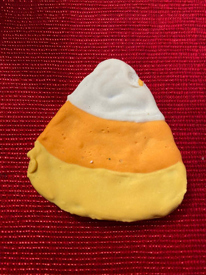 Organic Halloween dog cookie shaped like candy corn with white, orange, and yellow icing on red background