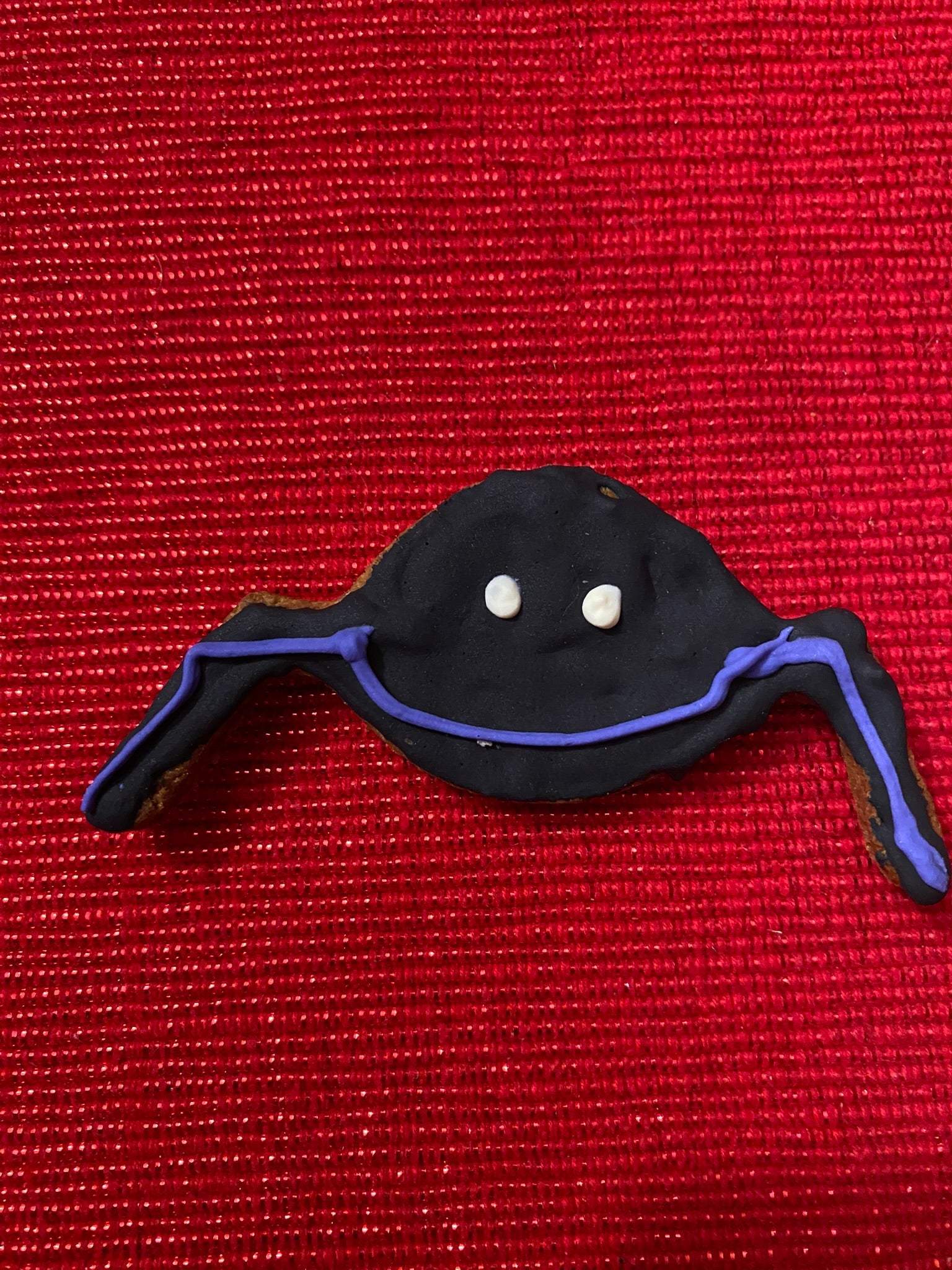 Organic Halloween dog cookie shaped like a ghost with purple accents on red background